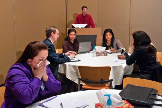 Woman sitting alone at a table covering her cough with a tissue during a conference.