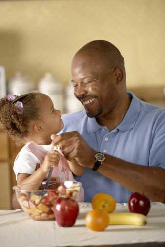 Dad and daughter sitting at table with apples and oranges