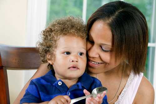 Toddler son holding a spoon sitting in mom's lap