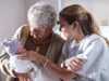 A mother introduces her newborn baby to her grandmother in a hospital recovery room.