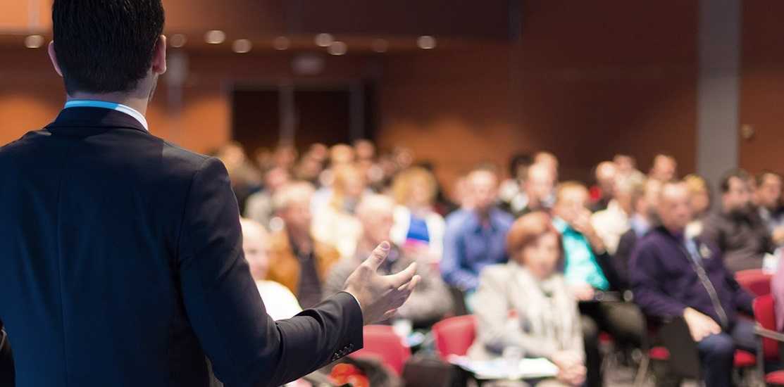 Image of a conference with speaker and participants.