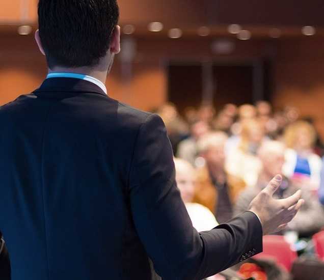 Image of a conference with speaker and participants.