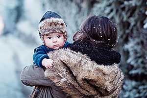 Alaska Native mother carrying her infant son outside in a wintry wonderland