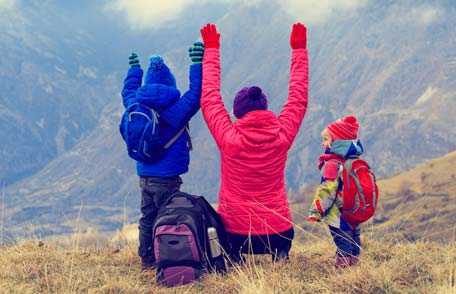 Una madre y sus hijos caminando y levantando las manos hacia arriba