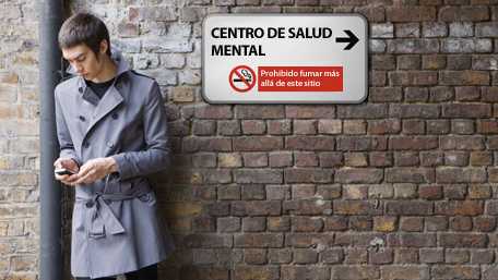 Hombre enviando un mensaje de texto con su celular, afuera de una institución de salud mental