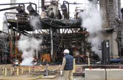 Trabajador que mira una planta manufacturera humeante