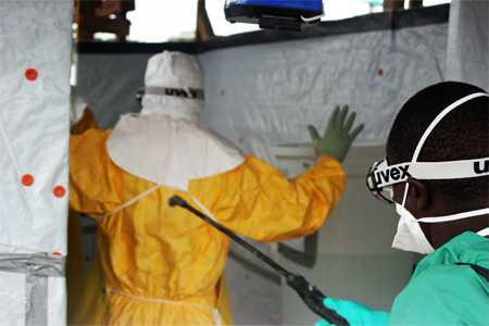 Clinician, assisted by a Médecins Sans Frontières staff member, following a protocol for decontamination before exiting an Ebola Treatment Unit.